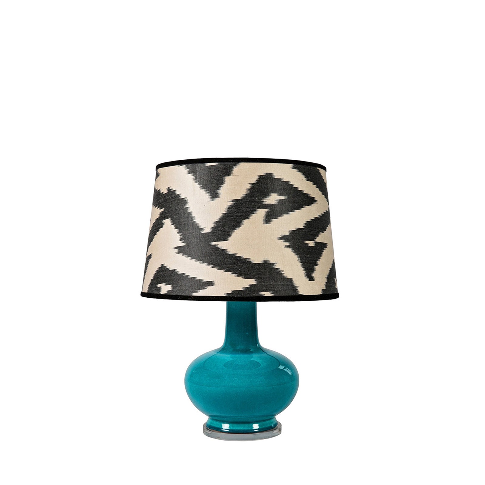 Turquoise table lamp with a patterned black and white shade on a white background