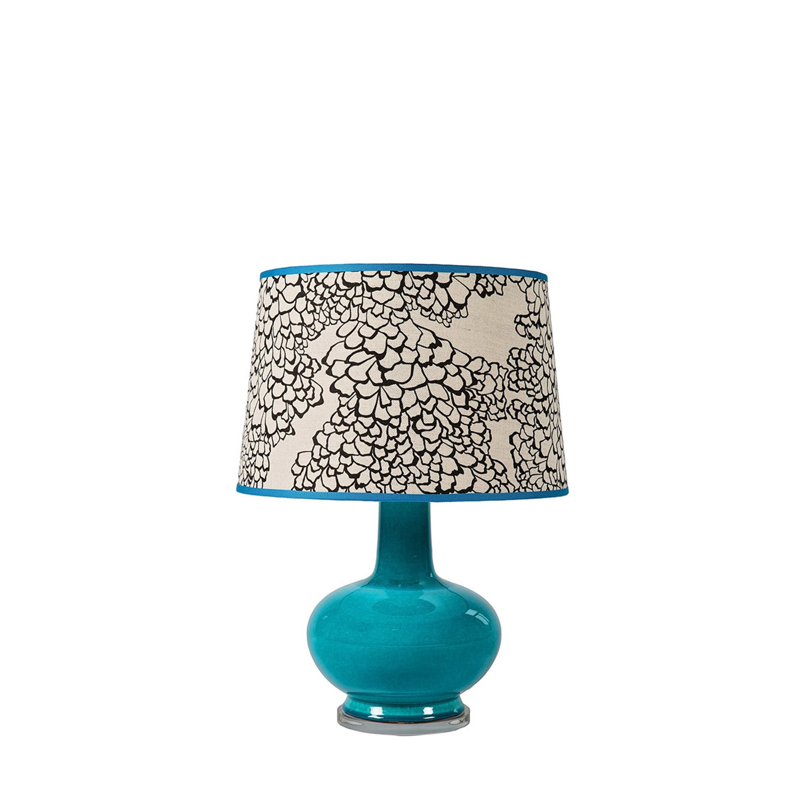 Turquoise table lamp with a patterned beige and black lampshade on a white background