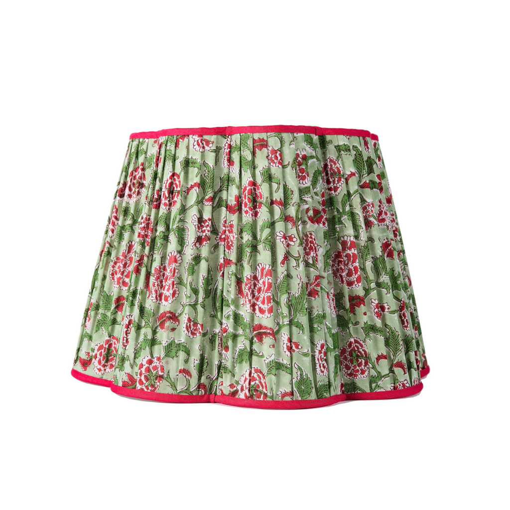 A gathered and fluted lampshade with a block printed cotton pattern, featuring red floral motifs on a green background and trimmed with a red border.